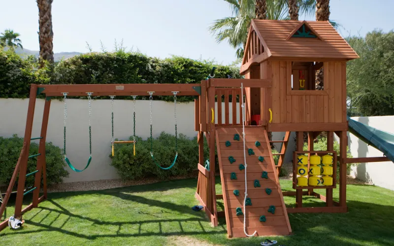 Wooden outdoor play equipment set for preschool children, featuring slide, climbing structure, and playhouse.