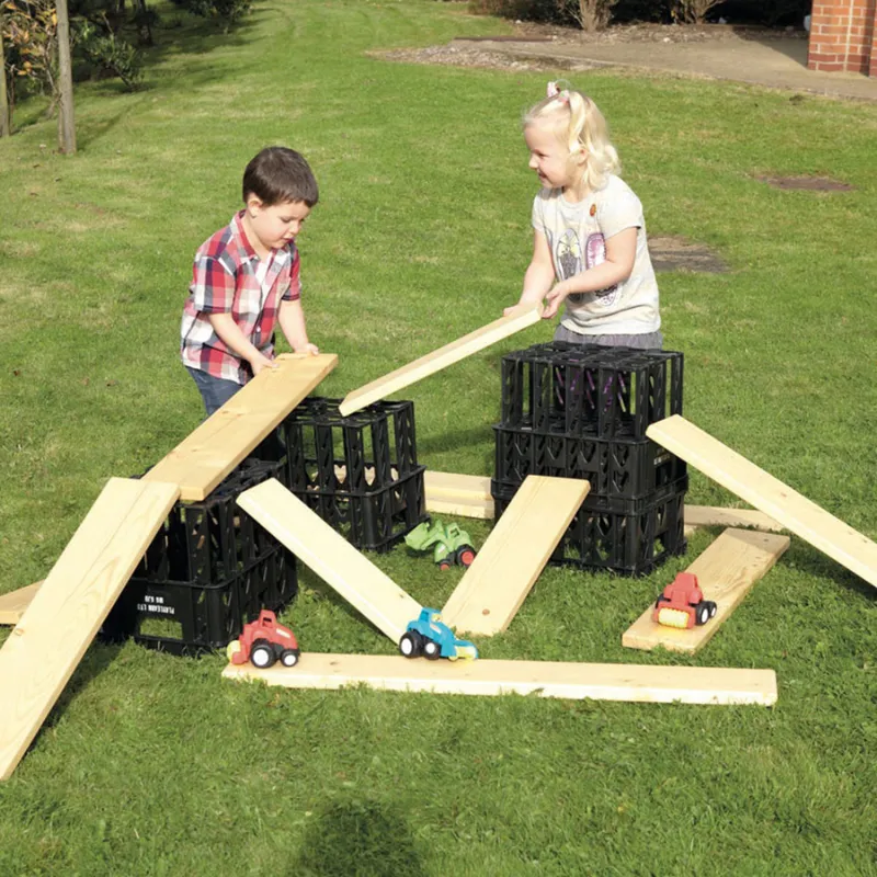 Children balancing and building with outdoor wooden planks and loose parts for preschool STEM design and gross motor play