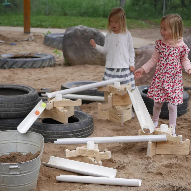 Children playing with outdoor engineering ramp kit using balls, tubes, and slopes to explore STEM motion experiments