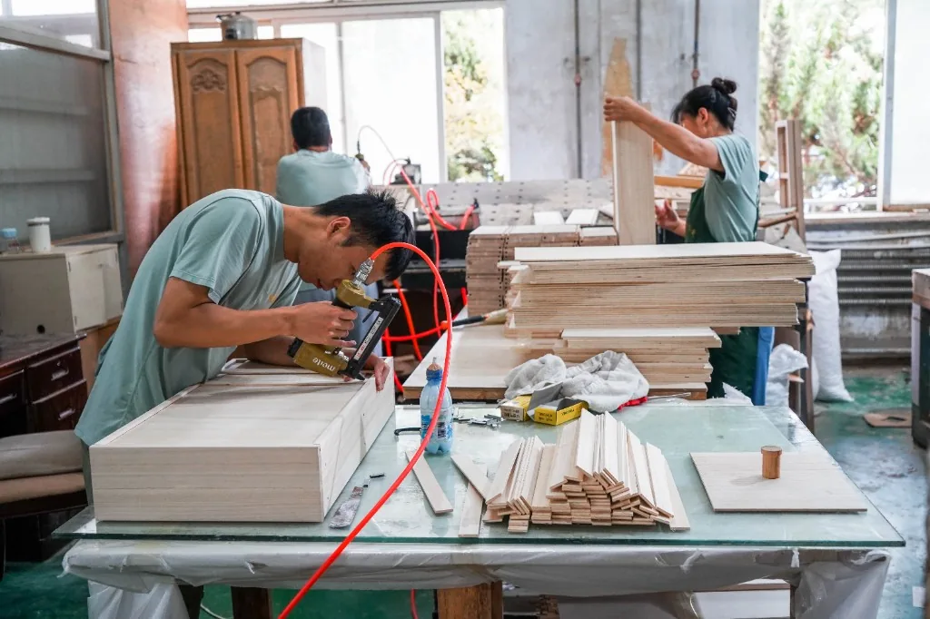 Workers assembling preschool cabinet parts on a bench in the Dalian factory