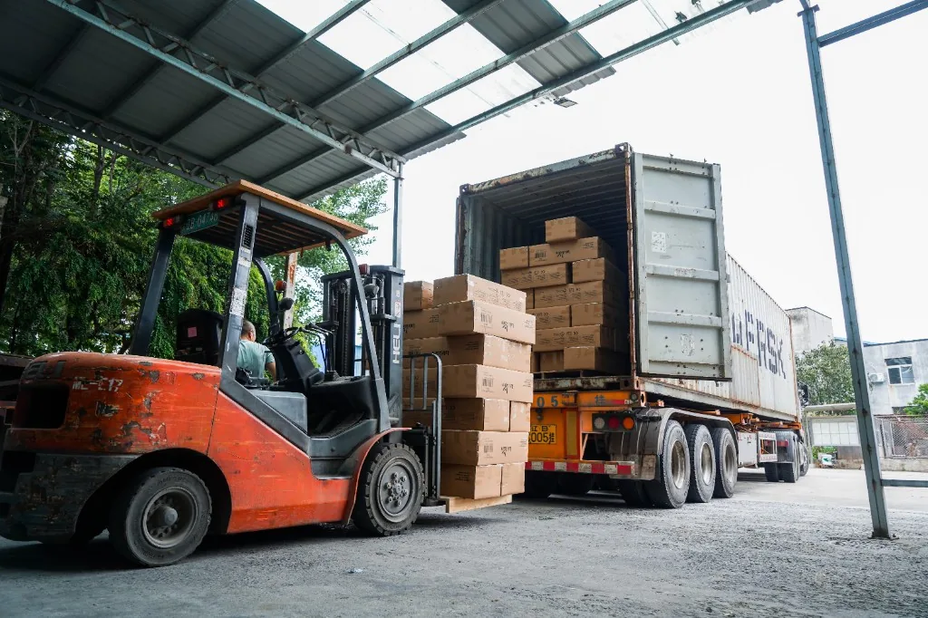 Forklift loading cartons of preschool furniture into an open shipping container at the factory