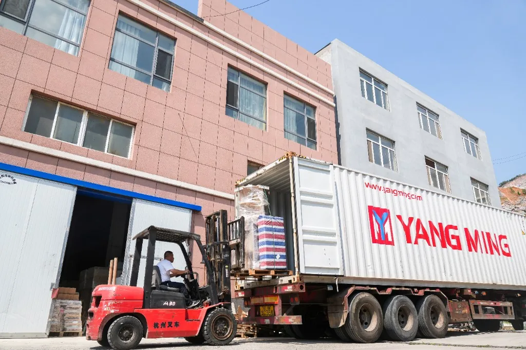 Forklift loading a pallet into a Yang Ming shipping container outside the West Shore factory