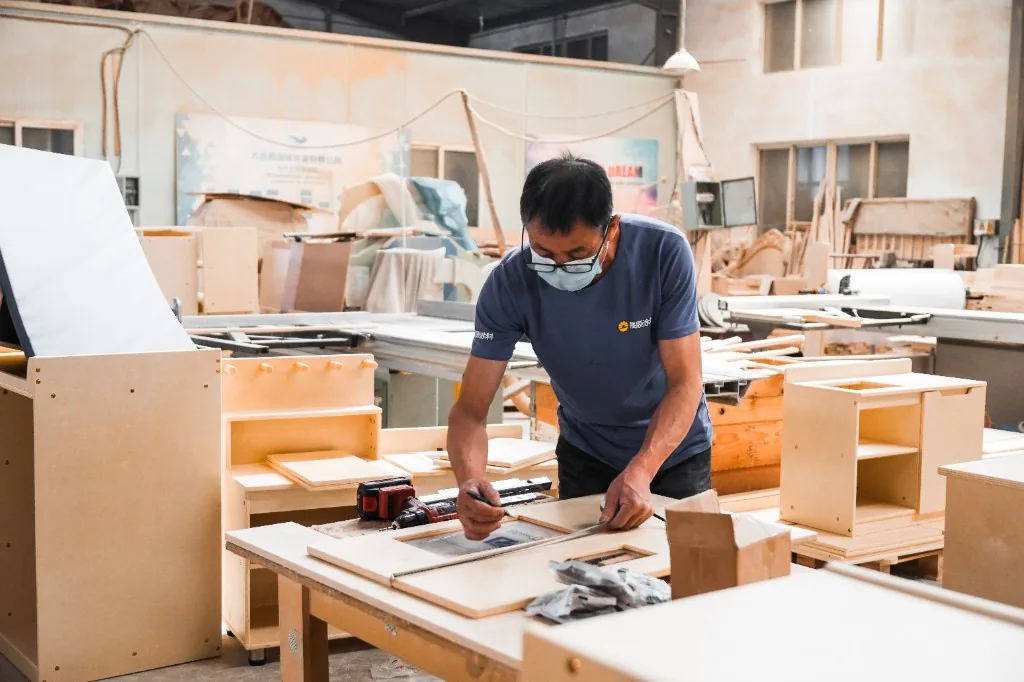 Factory worker marking a cabinet panel against the drawing in the Dalian workshop
