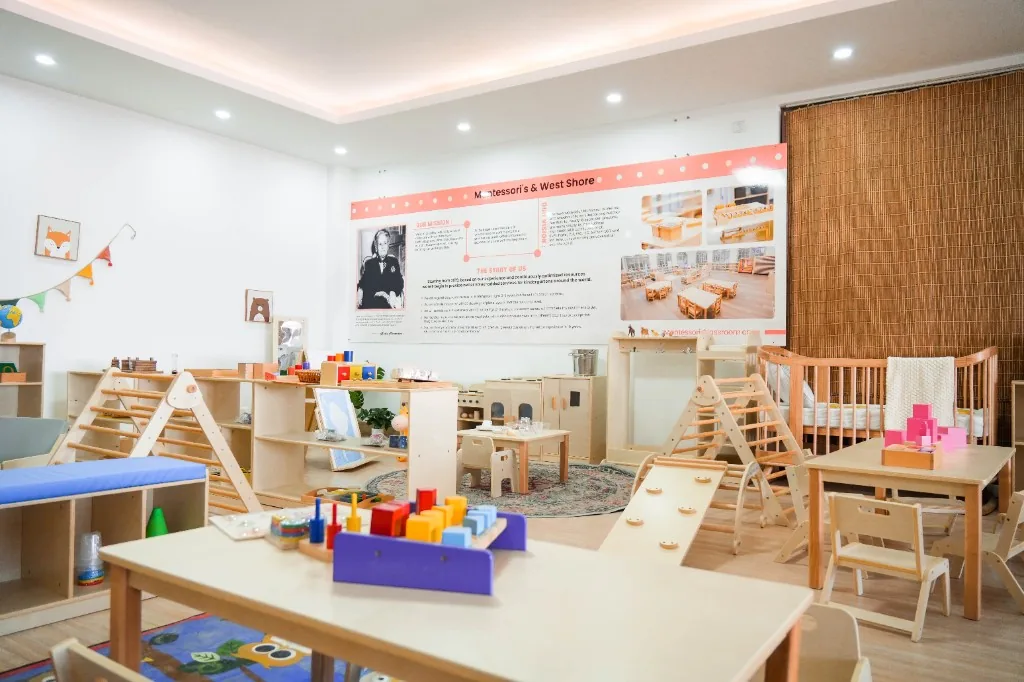 West Shore Montessori classroom with child-height tables, Pikler triangles, open shelves and a wall panel reading Montessori and Westshore
