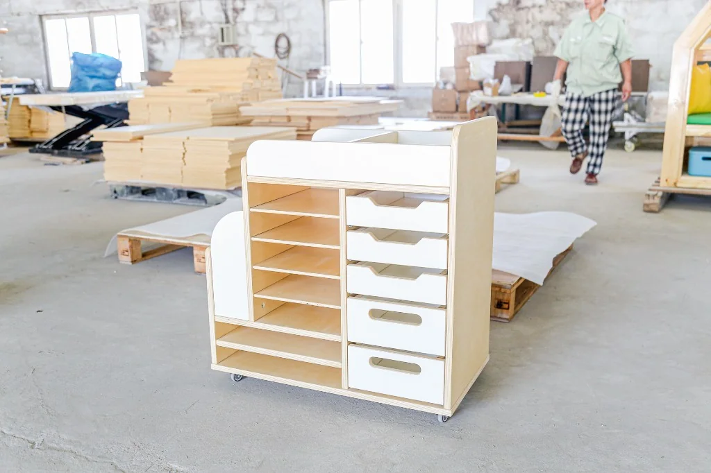 Birch plywood preschool changing station with open shelves, four white drawers and casters, photographed in the factory