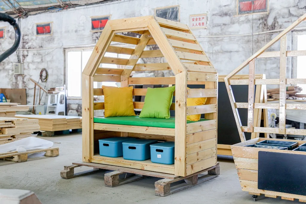 Solid pine house-shaped preschool reading nook with a green cushion, pillows and blue bins