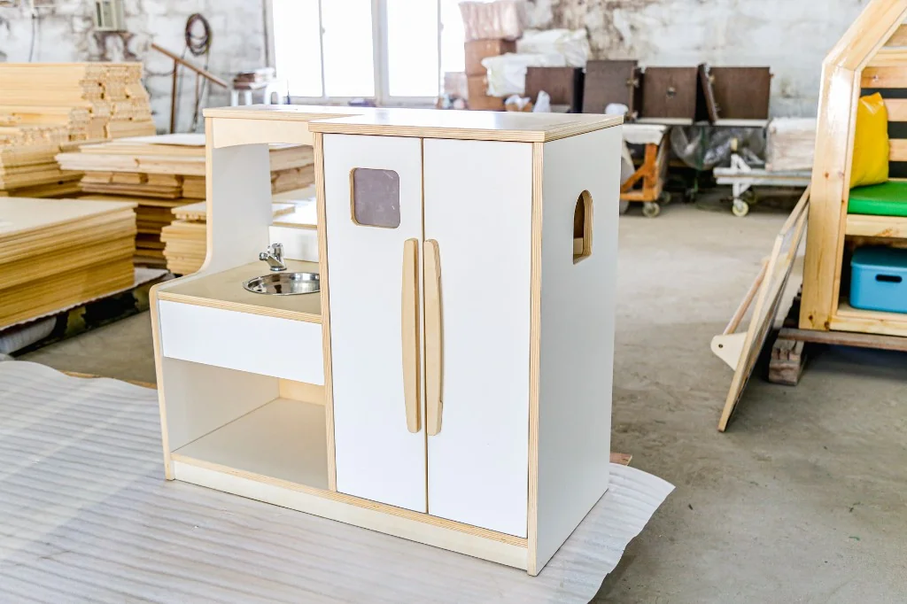 White preschool play kitchen unit with a stainless sink, fridge doors and wooden handles