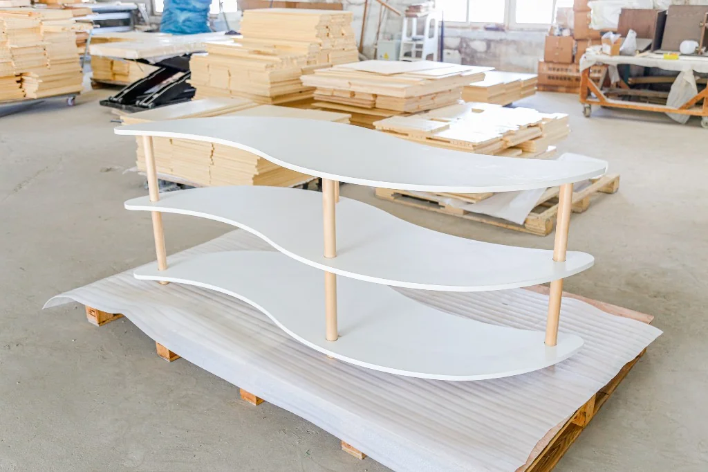 White laminate wave-shaped three-tier preschool display shelf on a factory pallet